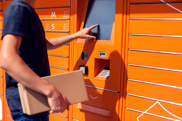 Man using automated self service post terminal machine or locker to deposit the parcel for storage