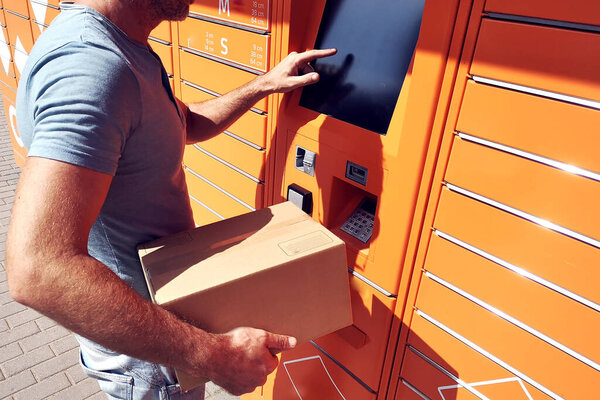 Man using automated self service post terminal machine or locker to deposit the parcel for storage
