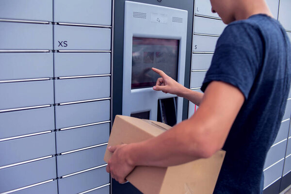 Man client using automated self service post terminal machine or locker to deposit a parcel for storage