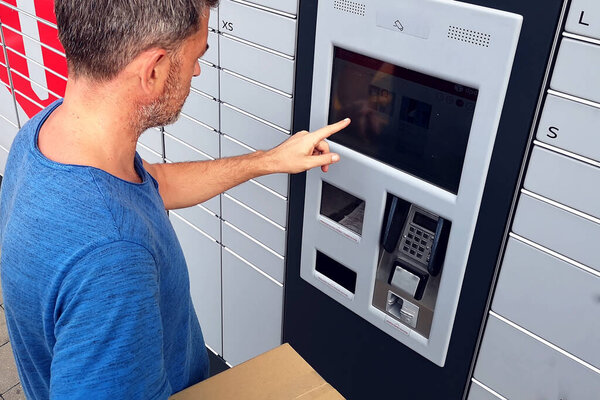 Man client using automated self service post terminal machine or locker to deposit a parcel for storage
