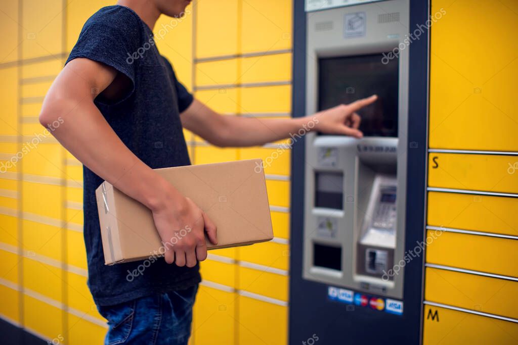 Man using automated self service post terminal machine or locker to deposit the parcel for storage