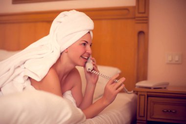 Teknoloji, iletişim ve insan konsepti. Genç bir kadın yatakta uzanıyor ve yatak odasında telefonunu kullanıyor.