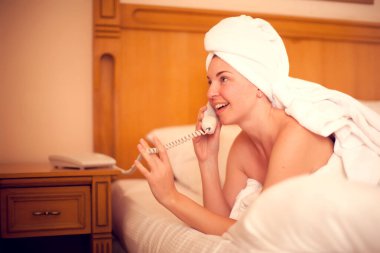 Teknoloji, iletişim ve insan konsepti. Genç bir kadın yatakta uzanıyor ve yatak odasında telefonunu kullanıyor.