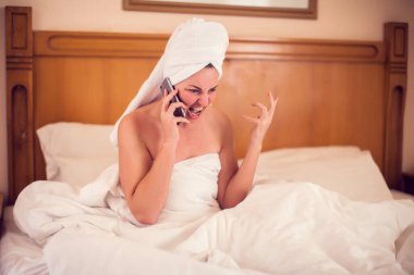 Teknoloji, iletişim ve insan konsepti. Yatakta yatıp evde telefonla konuşan öfkeli genç bir kadın.