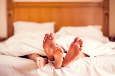 Yatakta çıplak ayaklı bir çift. Beyaz klanın altında yatan sevgi dolu bir çift.