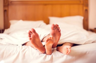 Yatakta çıplak ayaklı bir çift. Beyaz battaniyenin altında yatan sevgi dolu bir çift. İnsanlar ve yaşam tarzı kavramı