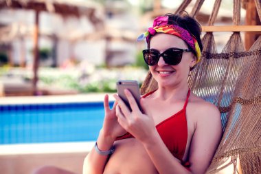 Tatil ve teknoloji. Kırmızı mayo giymiş, hamakta bilardo oynayan genç ve güzel bir kadın..