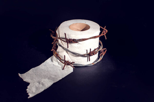 Toilet paper with barbed wire around it on black background. People, healthcare and medicine concept.