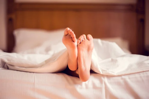 Close up of woman\'s feet in a bed under blanket. People and lifestyle concept