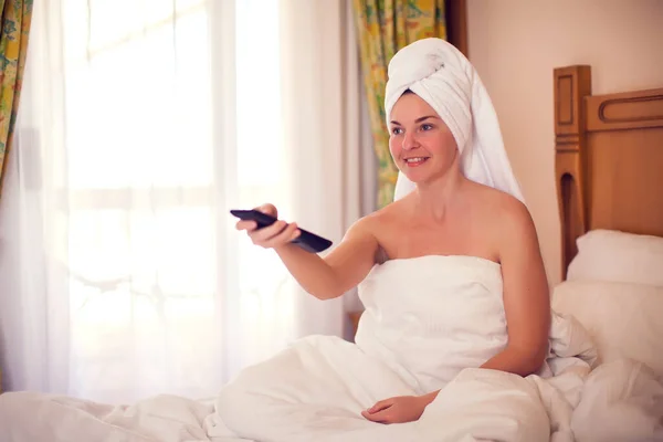 Young woman in bed watching TV in the room. Switching tv channels. People and lifestyle concept