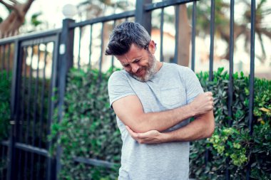 Sokakta dirsek ağrısı çeken bir adam. Halk, sağlık ve tıp konsepti