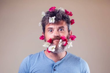 Sakalında ve saçında çiçekler olan yakışıklı, gülümseyen bir adam. İnsanlar, duygular, yaz ya da bahar konsepti