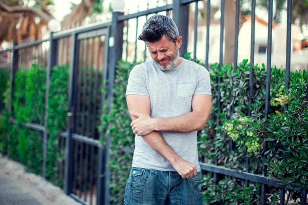 Sokakta dirsek ağrısı çeken bir adam. Halk, sağlık ve tıp konsepti