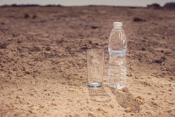 沙漠中沙滩上的玻璃杯和一瓶水 炎热和干旱的概念 — 图库照片