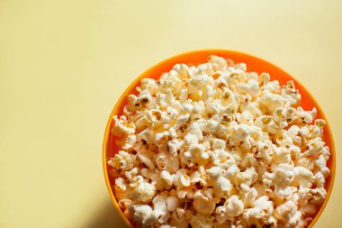 Sarı arka planda izole edilmiş patlamış mısırlı bir turuncu kase. Yiyecek konsepti