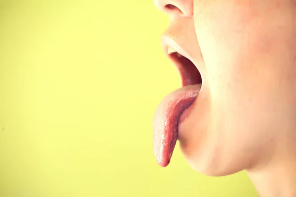 年轻女子在黄色背景上露出舌头的侧影 — 图库照片