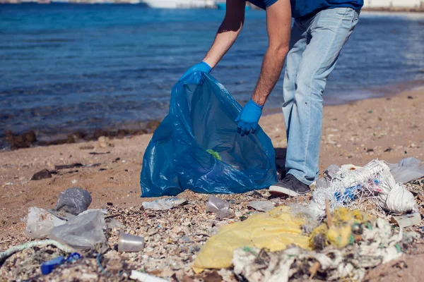 穿着蓝色T恤 提着大包垃圾在海滩上捡垃圾的人志愿工作 环境污染概念 — 图库照片
