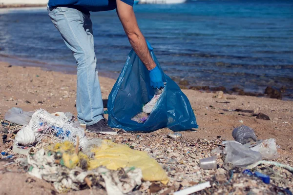 穿着蓝色T恤 提着大包垃圾在海滩上捡垃圾的人志愿工作 环境污染概念 — 图库照片
