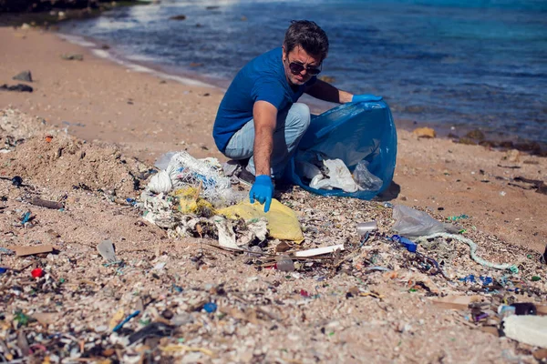 ビーチでゴミ収集のための大きな袋と青のTシャツの男ボランティア 環境汚染の概念 — ストック写真
