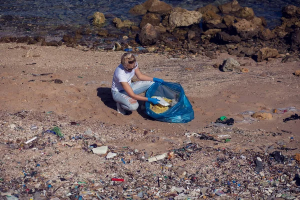 ビーチでゴミを集める大きな青い袋の白いTシャツの女性ボランティア 環境汚染の概念 — ストック写真