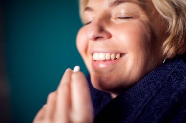 Happy smiling woman taking a pill or vitamine. People, healthcare and medicine concept