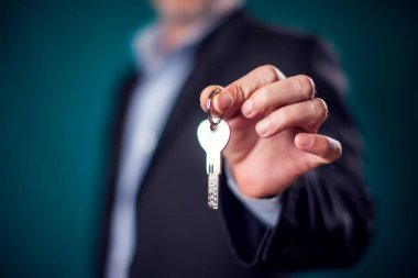 Businessman in suit holding house key in hand. Mortgage, credit or property concept