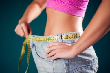 Woman wearing big size jeans with meter on the belt. Weight loss, fitness and diet concept