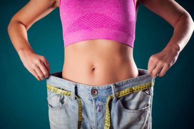 Woman wearing big size jeans with meter on the belt. Weight loss, fitness and diet concept