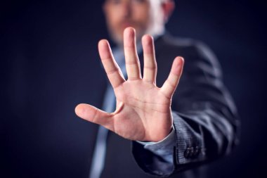 Businessman in suit showing stop sign with hands in front of black background