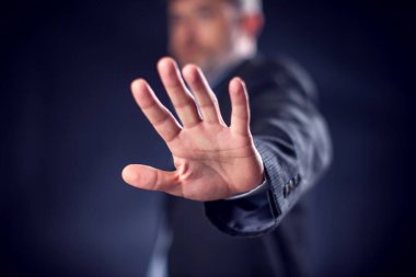 Businessman in suit showing stop sign with hands in front of black background