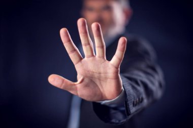 Businessman in suit showing stop sign with hands in front of black background