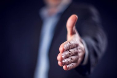 Businessman in suit showing handshake at camera in front of black background