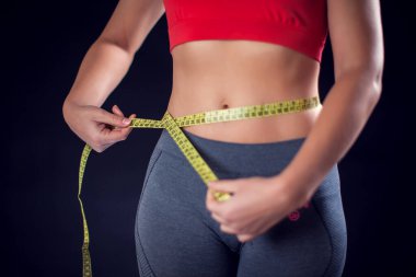 Woman in red top measuring her waist with meter. Sport, lifestyle and health concept
