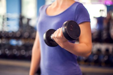 Woman in blue shirt with short hair training with dumbbells in the gym. People, fitness and health concept