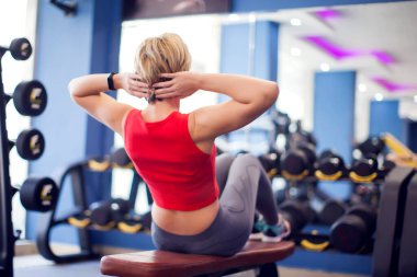 Woman in red top with short blond hair training abs in gym. People, fitness and lifstyle concept