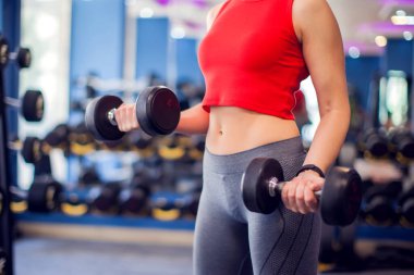 Woman in red top with short blond hair training bicep in gym. People, fitness and lifstyle concept