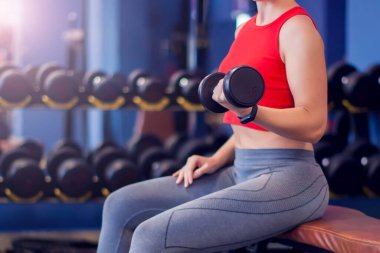Woman in red top with short blond hair training bicep in gym. People, fitness and lifstyle concept