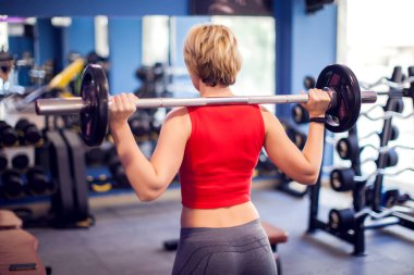 Woman in red top with short blond hair preparing to do squats in gym. People, fitness and lifstyle concept