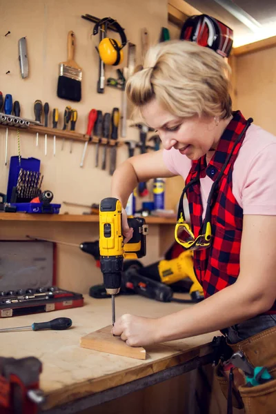 Young smiling handy woman with short blond hair working with screwdriver.