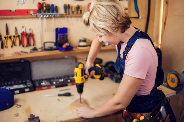 Young smiling handy woman with short blond hair working with screwdriver.