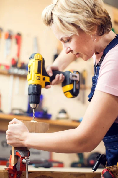 Young smiling handy woman with short blond hair working with screwdriver.