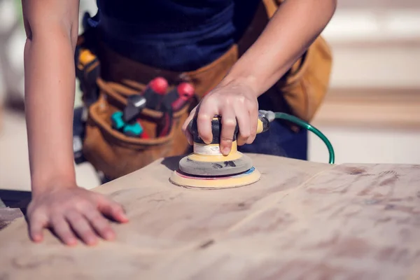 Young smiling handy woman with short blond hair sanding wooden surface.