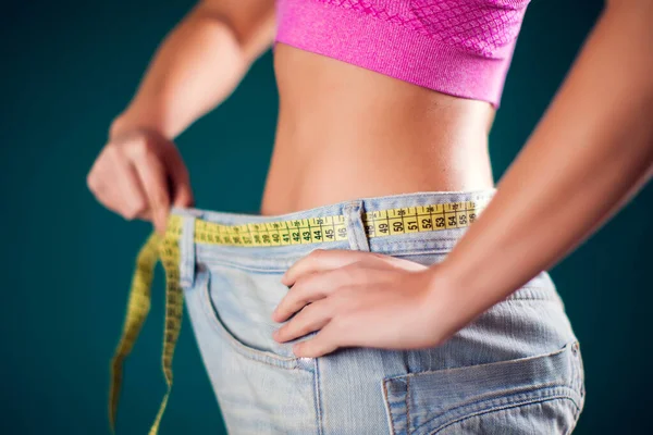 Woman wearing big size jeans with meter on the belt. Weight loss, fitness and diet concept