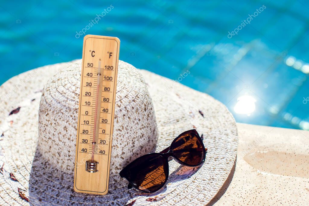 Woman's hat, thermometer and sunglasses lying beside the pool. Hot weather, summer and holiday concept