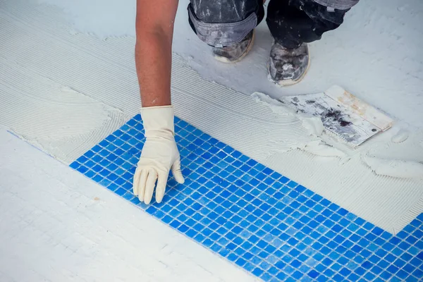 Worker laying tile in the pool. Pool repairing work.