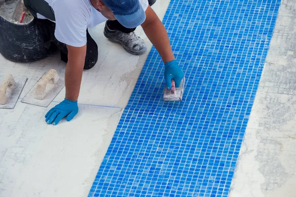 Worker laying tile in the pool. Pool repairing work.