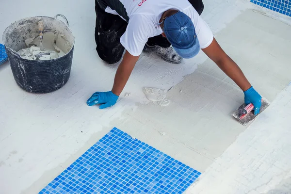 Worker laying tile in the pool. Pool repairing work.