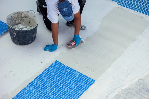 Worker laying tile in the pool. Pool repairing work.