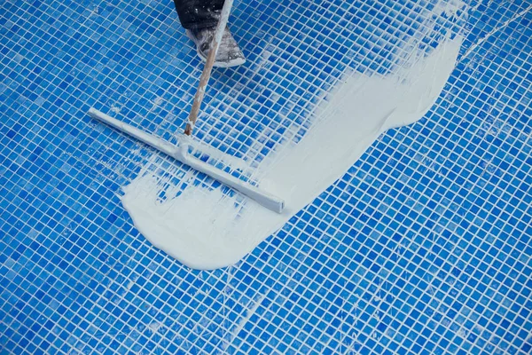Worker covering seames on the tile in the pool. Pool repairing work