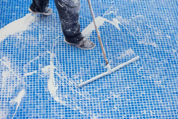 Worker covering seames on the tile in the pool. Pool repairing work